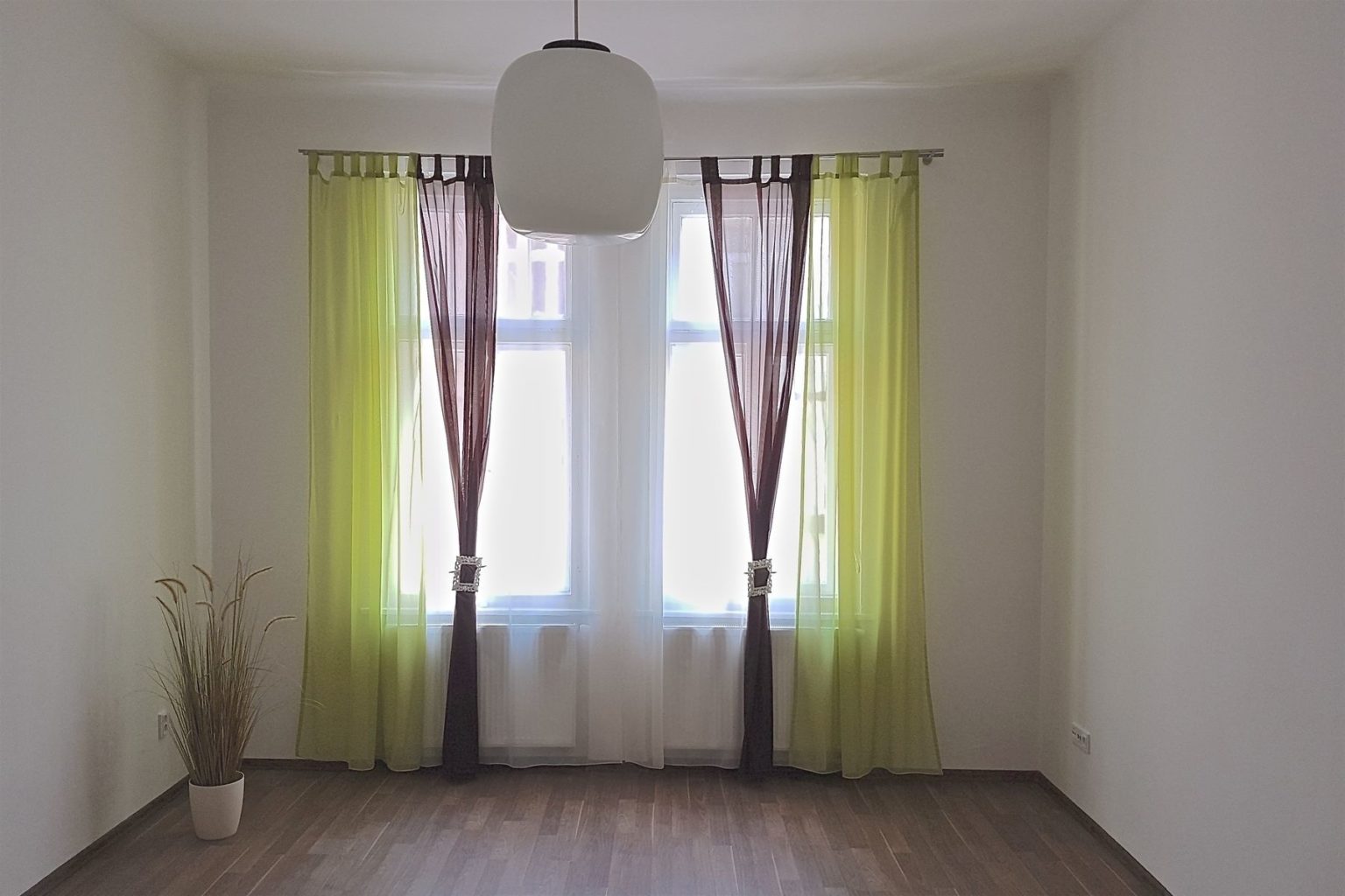 prázdná místnost s okenma zelenými a hnědými závěsy a bílé záclony