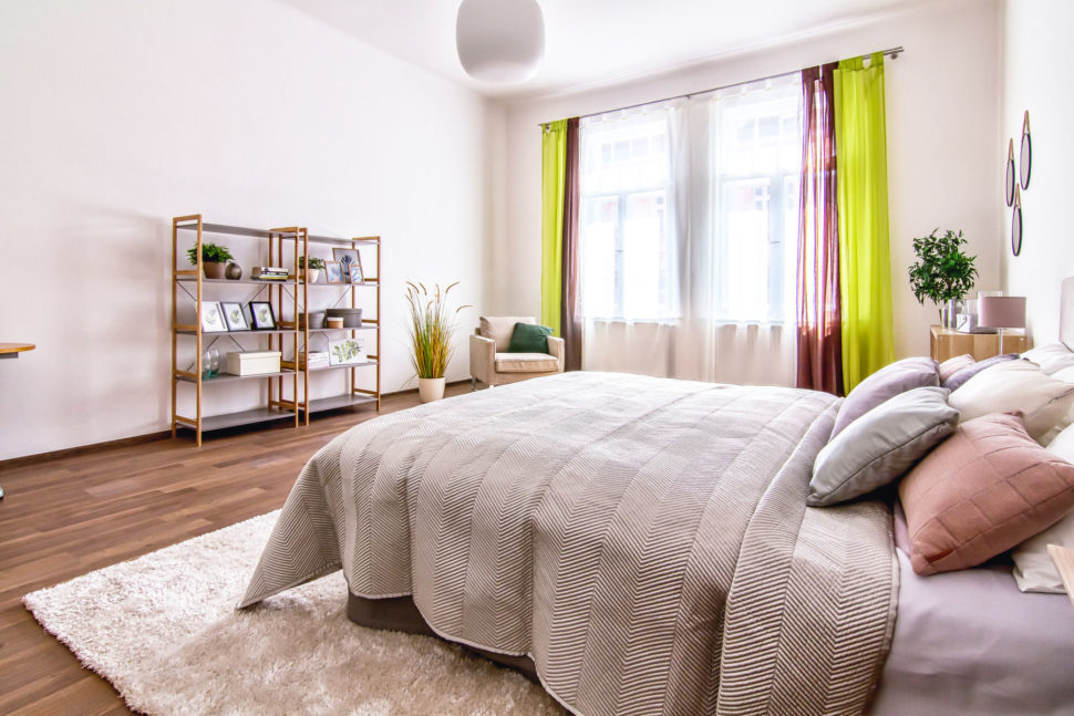 ložnice s postelí, dekorační polštáře, přehoz, koberec, křeslo a regály